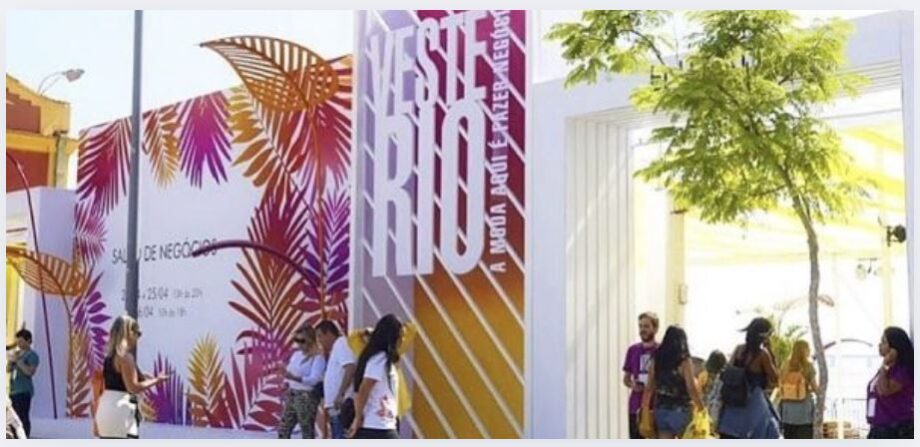 Imagem de uma entrada de evento com a placa "Feste Rio" e pessoas entrando, decoração colorida com elementos tropicais e grupo de visitantes.