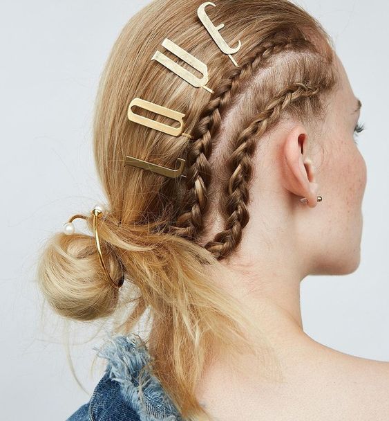 cabeleireira-penteado-kylie-jenner-letras-3d-douradas.webp Cabeleireira com penteado criativo usando letras 3D douradas numerando o cabelo e o nome de uma celebridade famosa, Kylie Jenner, visível em um penteado artístico e estilizado.